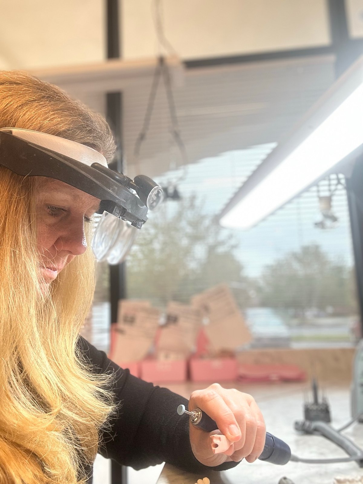 Carolynn Capps, CDT, working at the bench in magnifying loupes, finishing a restoration by hand