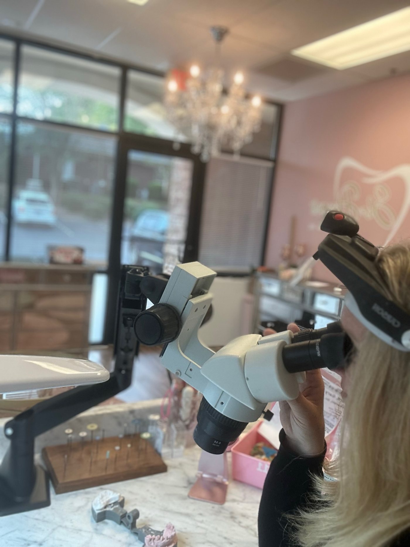Carolynn at the microscope in the She Designs studio, with the logo on the pink wall behind her